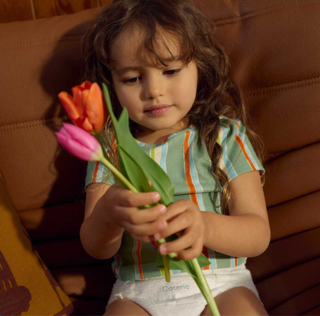 A little girl wearing diapers is admiring a bouquet of flowers.